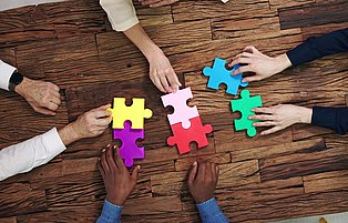 Mehrere Hände spielen mit großformatigen Puzzlestücken